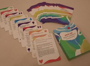 Beispielkarten eines Kartensets in schräg gestaffelter Anordnung sowie einer zweiten Reihe der Kartenrückseiten, die farbig gestaltetet sind.  Schachtel, die die Karten enthält.  Der Deckel des Kartensets trägt die Aufschrift: Wege zur Achtsamkeit